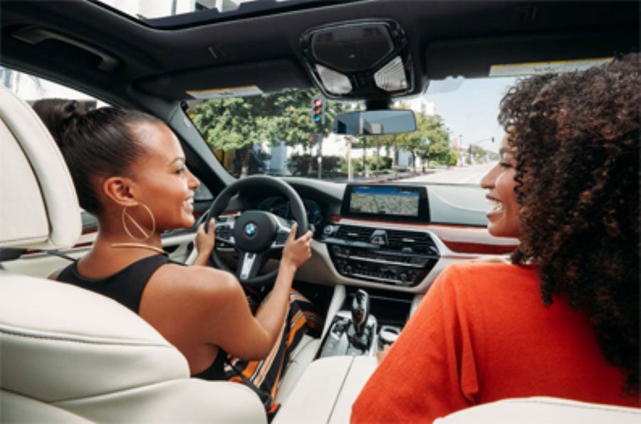 Two women (driver and passenger) smile at each other inside a BMW.